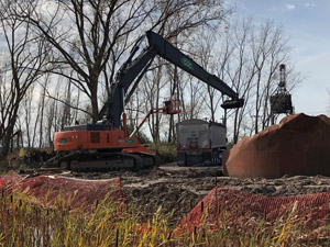 November 2019 - Site 108 - view looking south.  Long stick excavator loading stabilized tar; manlift used to assist excavator operator in placing the load evenly in the bed of the trailer. Tank 3 is visible on the right side.